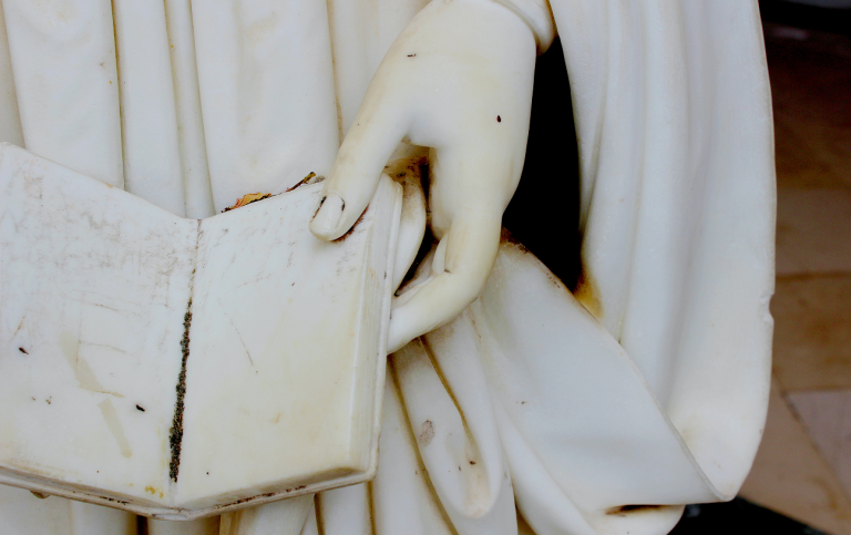 Detalj av marmorstaty, hand som håller en öppen bok. Foto: Unsplash 